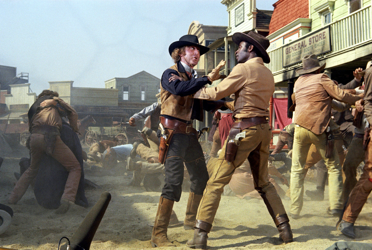 Full shot of Gene Wilder as Jim and Cleavon Little as Bart, wearing hats, standing in street while cowboys fight. NOTE: boom microphone visible at bottom left..PHOTOGRAPHS TO BE USED SOLELY FOR ADVERTISING, PROMOTION, PUBLICITY OR REVIEWS OF THIS SPECIFIC MOTION PICTURE AND TO REMAIN THE PROPERTY OF THE STUDIO. NOT FOR SALE OR REDISTRIBUTION. ALL RIGHTS RESERVED.