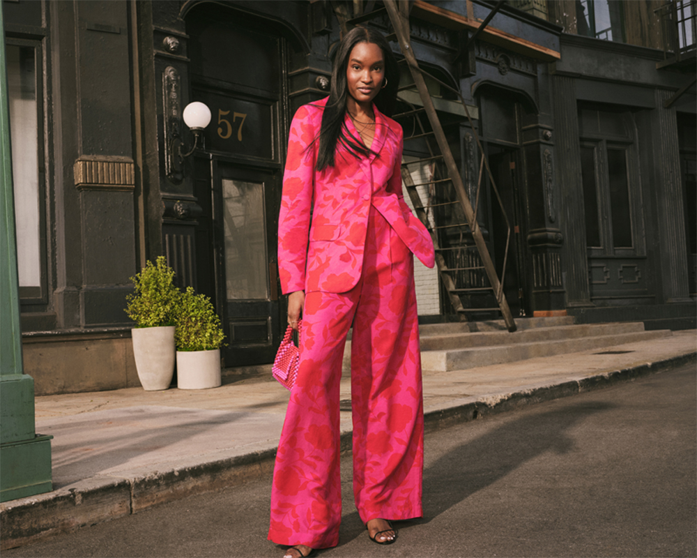 woman posing in a coordinated blazer and trousers set from kate spade while holding a beaded handbag