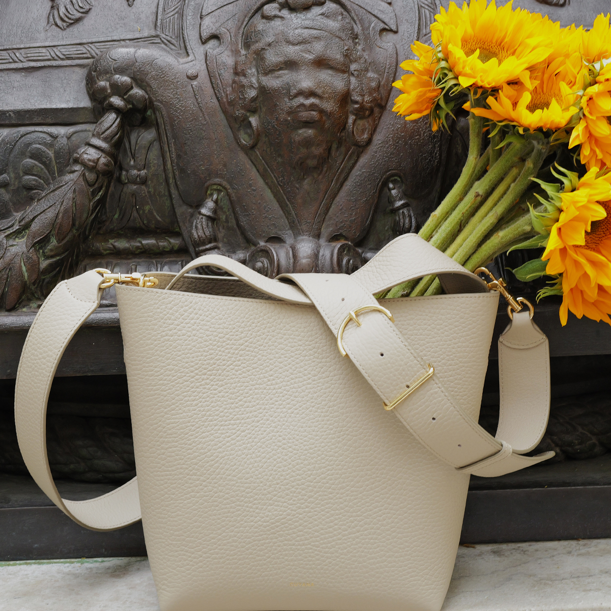 WWD shopping editors test Cuyana's Linea Bucket Bag with flowers in it on a ledge of a New York City building with statue in the background