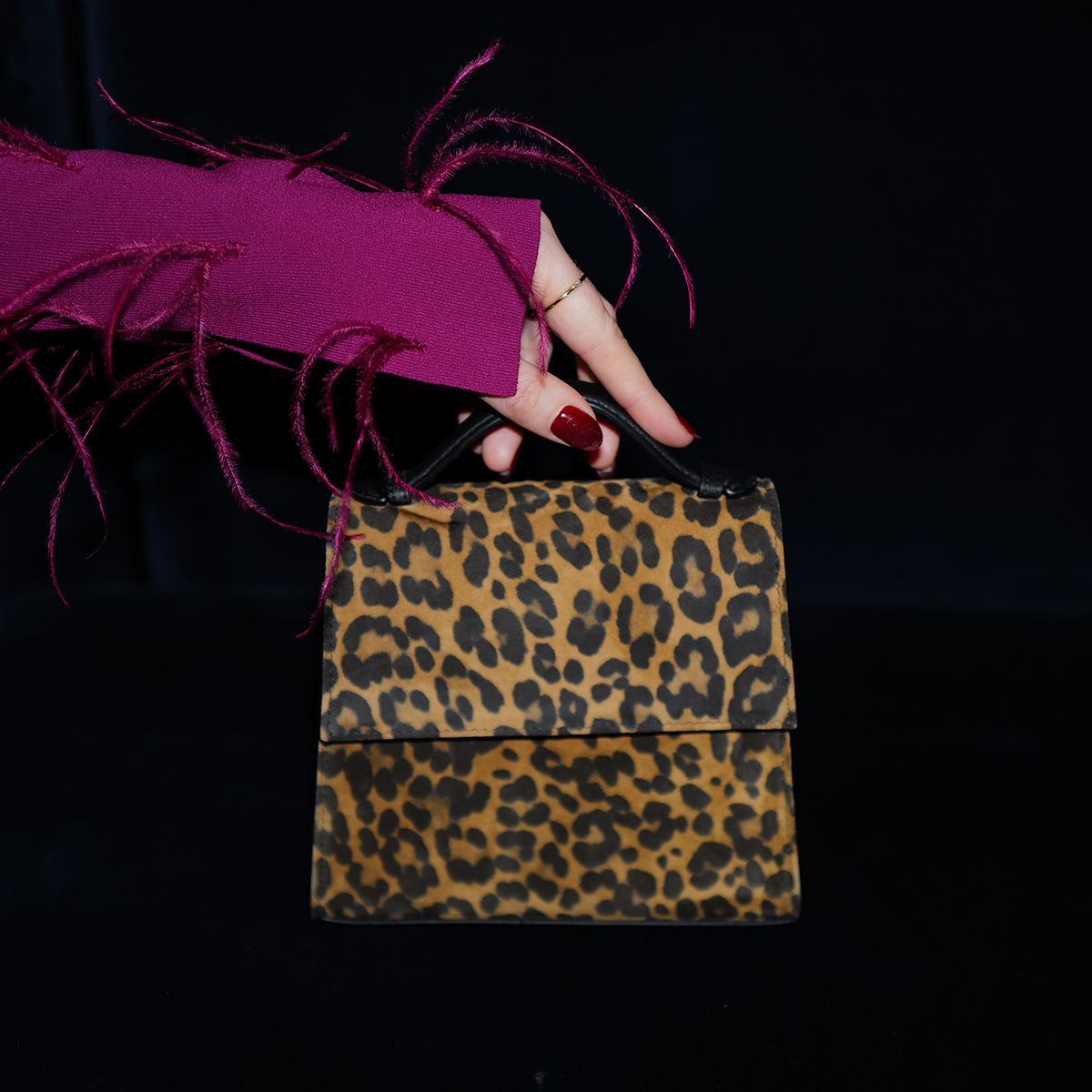 WWD shopping editors test Hunting Season's top handle bag in leopard on black velvet couch with hand reaching out holding it