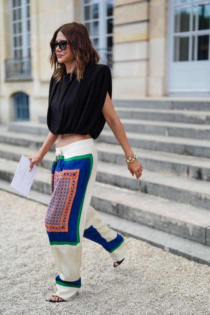 PARIS, FRANCE - JUNE 24: Christine Centenera wears black sunglasses, black cropped high shoulders shirt, diamond and gold bracelet, a silver ring, white dark green and blue orange pattern/print Celine pajama loose pants, black strappy heels leather shoes, outside Dior, during the Paris Haute Couture Week Fall/Winter 2024-2025 on June 24, 2024 in Paris, France. (Photo by Edward Berthelot/Getty Images)
