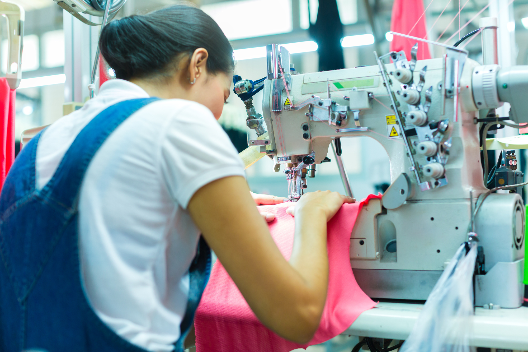 Asian Seamstress or worker in an Asian textile factory sewing with a industrial sewing machine, she is very accurate