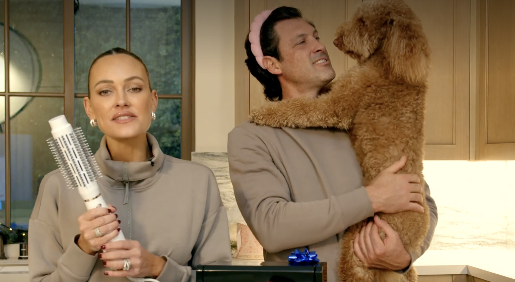 Peta Murgatroyd and Maksim Chmerkovskiy talking during a livestream while holding up their dog and a hair dryer brush